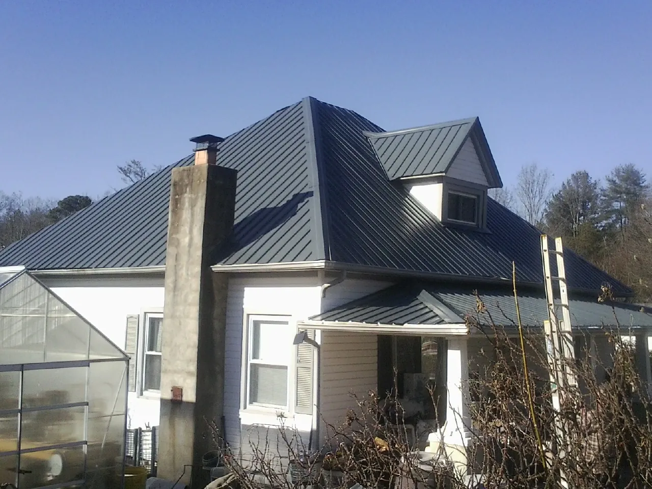 Dark blue standing seam metal roof on a white farmhouse with dormer — Slate & Tile Roof Repair by Roofing Brothers in Melvindale