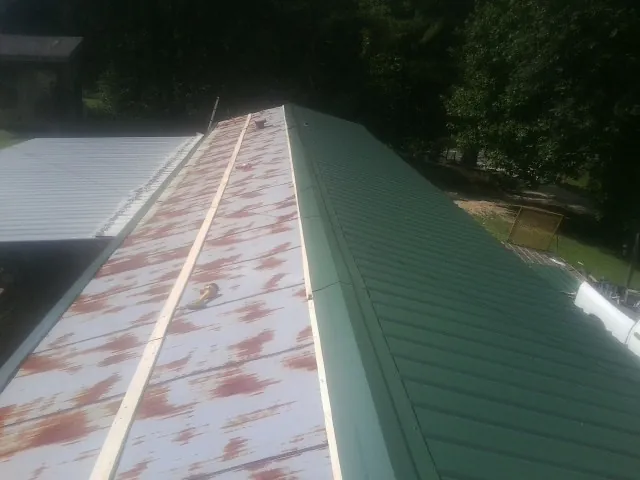 Old rusted panels beside newly installed green metal roofing — Wind Damage Roof Repair by Roofing Brothers in Melvindale