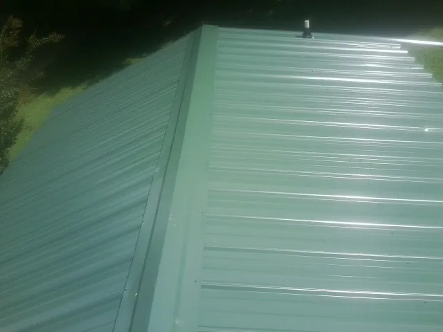 New green metal panels meeting at the ridge of a roof — Flat Roof Repair work by our crew in Melvindale