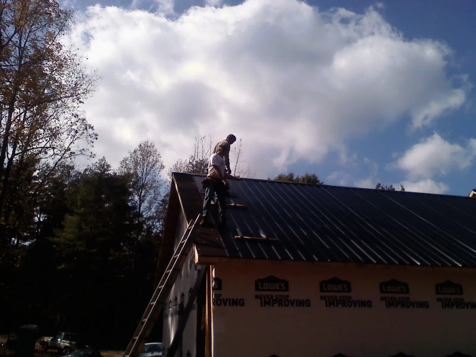 Roofer fastening dark metal panels high against a cloudy sky, from a Roof Inspection job in Melvindale